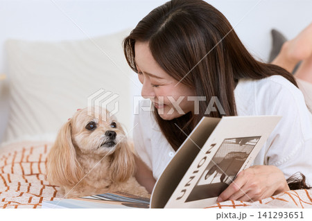 ベッドの上で愛犬と一緒に雑誌を読む笑顔の若い女性 ベッドの上で愛犬と一緒に雑誌を読む笑顔の若い女性 141293651
