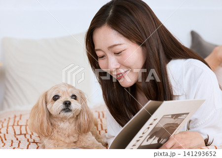 ベッドで愛犬と一緒に雑誌を読む笑顔の若い女性 ベッドで愛犬と一緒に雑誌を読む笑顔の若い女性 141293652