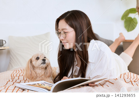 ベッドの上で愛犬と一緒に雑誌を読むメガネの若い女性 ベッドの上で愛犬と一緒に雑誌を読むメガネの若い女性 141293655