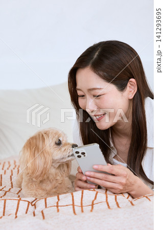 スマートフォンを見ながら愛犬と寛ぐ笑顔の若い女性 141293695