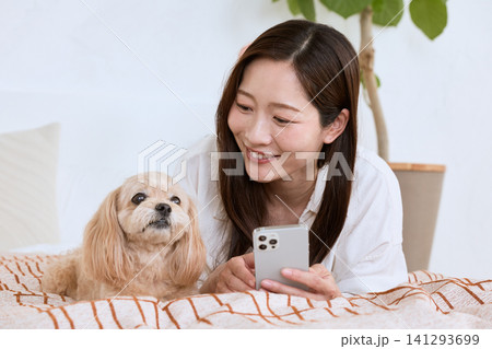 スマートフォンを見ながら愛犬とくつろぐ笑顔の若い女性 スマートフォンを見ながら愛犬とくつろぐ笑顔の若い女性 141293699