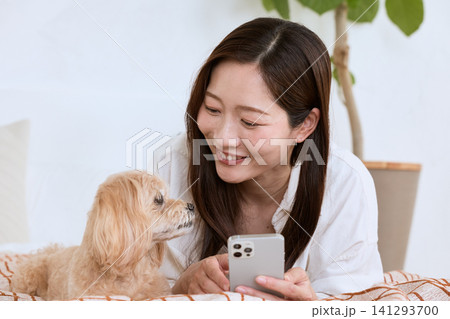 リビングで愛犬と一緒にスマートフォンを見る笑顔の若い女性 141293700