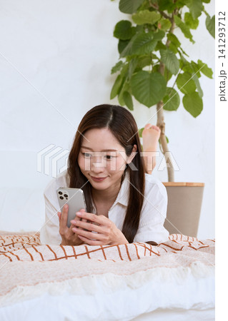 ソファでスマートフォンを見て微笑む若い女性 ソファでスマートフォンを見て微笑む若い女性 141293712