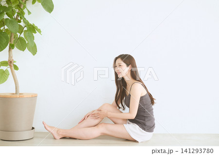 白い壁の前で座り脚のケアをする長髪の若い女性 141293780