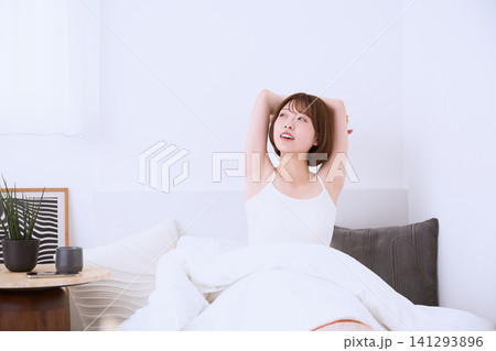 朝ベッドの上で伸びをする笑顔の若い女性 朝ベッドの上で伸びをする笑顔の若い女性 141293896