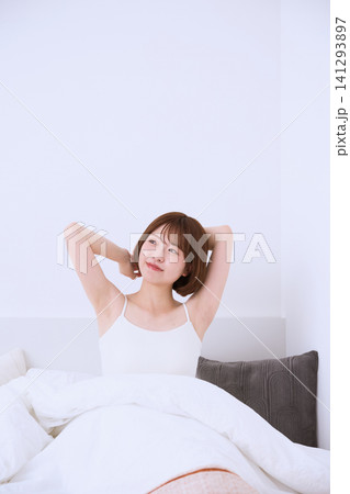 ベッドの上でストレッチをする白いタンクトップの若い女性 ベッドの上でストレッチをする白いタンクトップの若い女性 141293897