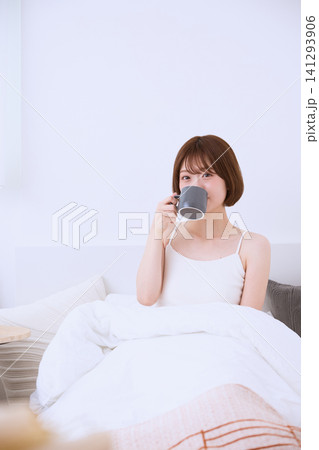ベッドに座りコーヒーを飲む白いタンクトップの若い女性 141293906