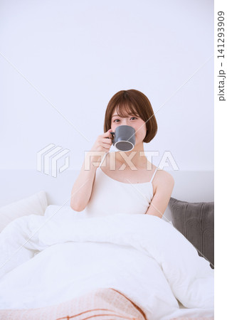ベッドの上でマグカップを持ちコーヒーを飲む若い女性の朝 141293909