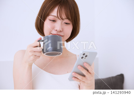 スマートフォンを見ながらコーヒーを飲む若い女性 スマートフォンを見ながらコーヒーを飲む若い女性 141293940