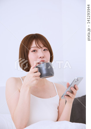 コーヒーを飲みながらスマートフォンを操作する若い女性 141293944
