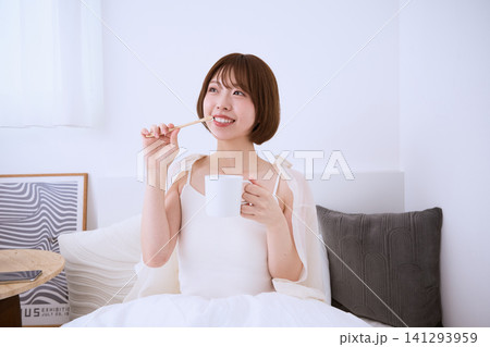 ベッドの上で歯磨きをする笑顔の若い女性の朝の風景 ベッドの上で歯磨きをする笑顔の若い女性の朝の風景 141293959