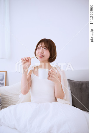 ベッドに座り歯ブラシとコップを持つ朝の若い女性 ベッドに座り歯ブラシとコップを持つ朝の若い女性 141293960