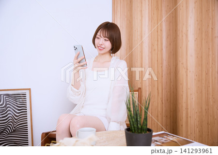 リビングでスマートフォンを見て微笑む若い女性 リビングでスマートフォンを見て微笑む若い女性 141293961