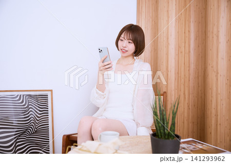 カフェでスマートフォンを見て微笑む白い服の若い女性 カフェでスマートフォンを見て微笑む白い服の若い女性 141293962