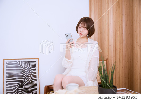 自宅でスマートフォンを見るショートヘアの若い女性 自宅でスマートフォンを見るショートヘアの若い女性 141293963