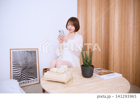 おしゃれな部屋でスマートフォンを見る白い服の若い女性 おしゃれな部屋でスマートフォンを見る白い服の若い女性 141293965