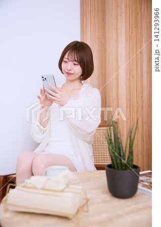 椅子に座りスマートフォンを見る白い服の若い女性 椅子に座りスマートフォンを見る白い服の若い女性 141293966