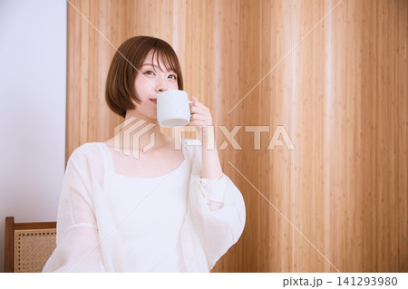 木目の壁の前でコーヒーを飲むショートヘアの若い女性 木目の壁の前でコーヒーを飲むショートヘアの若い女性 141293980