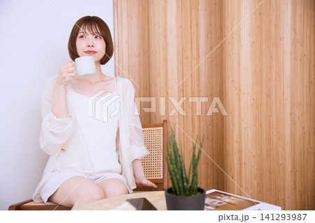 椅子に座りコーヒーを飲みながらくつろぐボブヘアの若い女性 椅子に座りコーヒーを飲みながらくつろぐボブヘアの若い女性 141293987