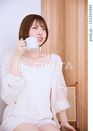 椅子に座りマグカップでコーヒーを飲む白い服の若い女性 椅子に座りマグカップでコーヒーを飲む白い服の若い女性 141293992