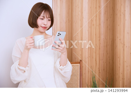スマートフォンを見ながらコーヒーを飲むボブヘアの若い女性 141293994