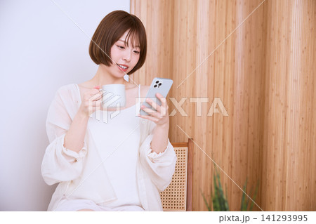 スマートフォンを見ながらコーヒーを飲むショートヘアの若い女性 スマートフォンを見ながらコーヒーを飲むショートヘアの若い女性 141293995