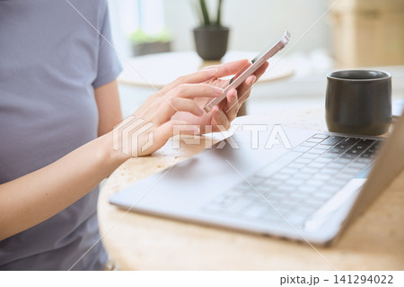 スマートフォンを操作する女性の手元とノートパソコン スマートフォンを操作する女性の手元とノートパソコン 141294022