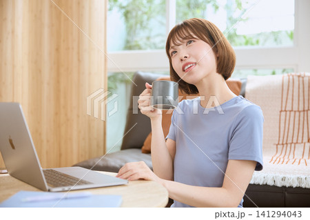 カフェ風リビングでコーヒーを飲みながらノートパソコンで作業する若い女性 141294043