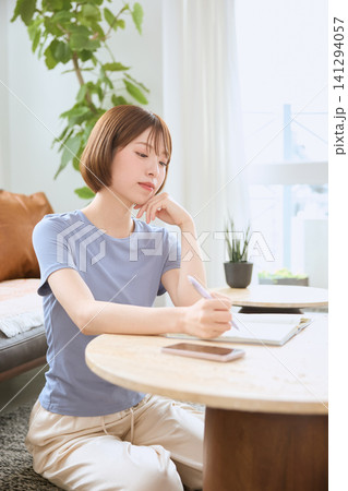 リビングでスマホを持ち悩む表情の若い女性 リビングでスマホを持ち悩む表情の若い女性 141294057