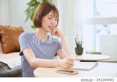 リビングでタブレットにスタイラスペンで書き込む笑顔の若い女性 リビングでタブレットにスタイラスペンで書き込む笑顔の若い女性 141294061