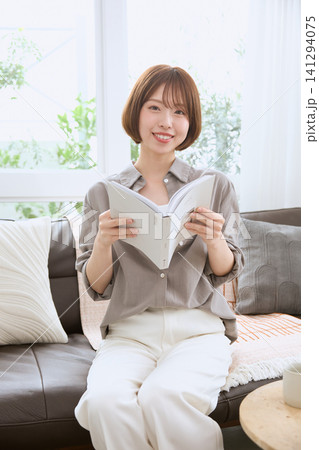 ソファに座って読書を楽しむ笑顔の若い女性 ソファに座って読書を楽しむ笑顔の若い女性 141294075