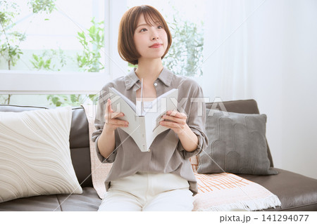 リビングのソファで本を読みながら考え事をする若い女性 リビングのソファで本を読みながら考え事をする若い女性 141294077