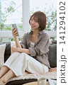 ソファでスマートフォンを見て笑顔の若い女性 141294102