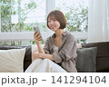 リビングのソファでスマートフォンを見て笑顔の若い女性 141294104