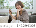 ソファでスマートフォンを見て笑顔の若い女性 141294106