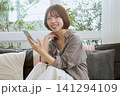ソファに座りスマートフォンを持って微笑む若い女性 141294109