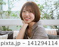 カフェで頬杖をつきながら笑顔を見せるボブヘアの若い女性 141294114