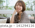 カフェのソファで頬杖をついて微笑むボブヘアの若い女性 141294116