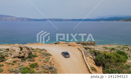 Horizontal high angle view of a gray car navigating a tight bend on a dusty coastal dirt road near Kissamos on Crete island in Greece with the deep blue sea behind Horizontal high angle view of a gray car navigating a tight bend on a dusty coastal dirt road near Kissamos on Crete island in Greece with the deep blue sea behind 141294523
