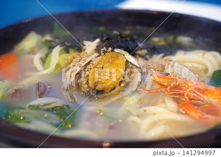 Delicious Korean noodle soup with mixed seafood, abalone, and prawns in a black bowl 141294997