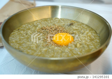 Korean abalone porridge topped with raw egg yolk and sesame seeds in a traditional brass bowl. Korean abalone porridge topped with raw egg yolk and sesame seeds in a traditional brass bowl. 141295101