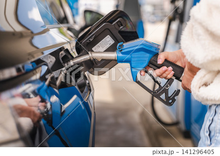 Closeup of woman holding fuel nozzle while refueling modern black car at petrol station during everyday transportation routine 141296405