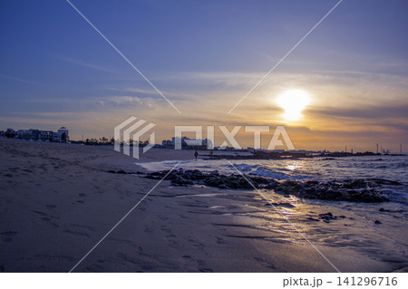 It is a beach scene with the sun setting. 141296716