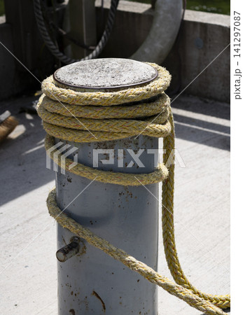 Yellow braided rope wrapped around a mooring bollard at a marina, conveying recreation on the water with a nautical vibe. 141297087