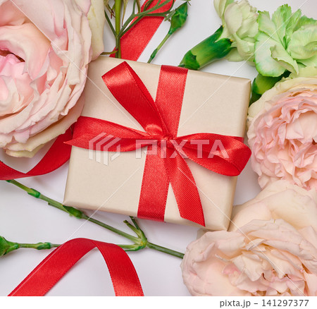 Festive arrangement with a gift box tied with a red ribbon, surrounded by soft pink roses Festive arrangement with a gift box tied with a red ribbon, surrounded by soft pink roses 141297377