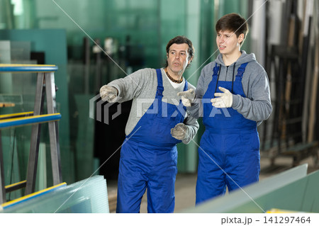 Adult and young man discussing work in glass factory Adult and young man discussing work in glass factory 141297464