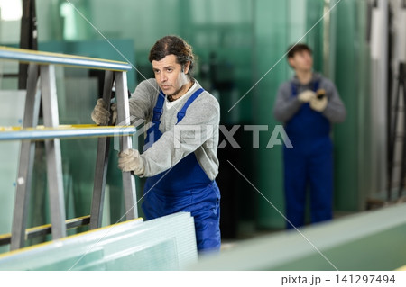 Man glazer employee in blue overall works in glass processing shop 141297494