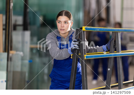 Girl glazer employee in blue overall works in glass processing shop Girl glazer employee in blue overall works in glass processing shop 141297509