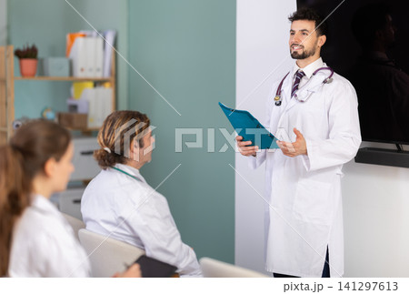Male doctor holding paper sheets explaining medical topic to students Male doctor holding paper sheets explaining medical topic to students 141297613