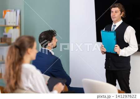 Male lecturer with folder addressed to attendees lecture Male lecturer with folder addressed to attendees lecture 141297622
